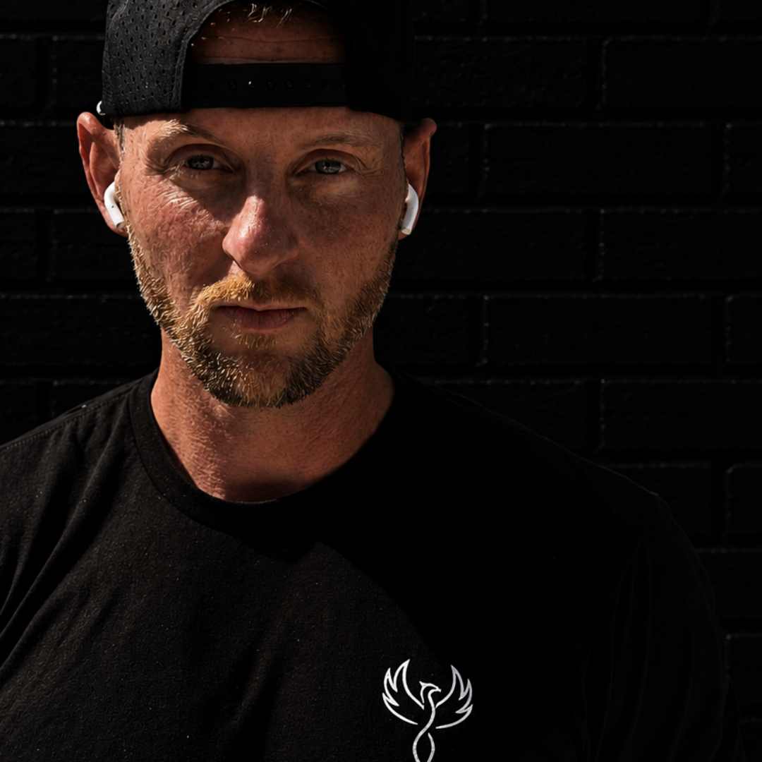 Man wearing a black cap and black t-shirt with a logo against a dark brick wall
